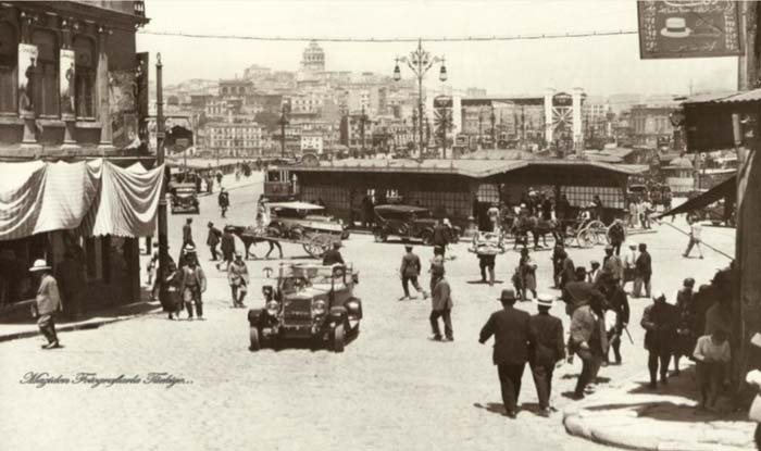 Yeni Cami basamaklarından 1928 yılında Eminönü... Bugünle kıyaslanırsa eğer, neredeyse hiç insan yok denebilir ortalıkta. Trafik belli bir doğaçlama ile akıyor… İnsanlar, 20'lerin otomobilleri, at arabaları... Kimi o tarafa kimi bu tarafa çevirm